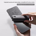 Hand holding a smartphone with a screen protector being applied, on a light gray background.